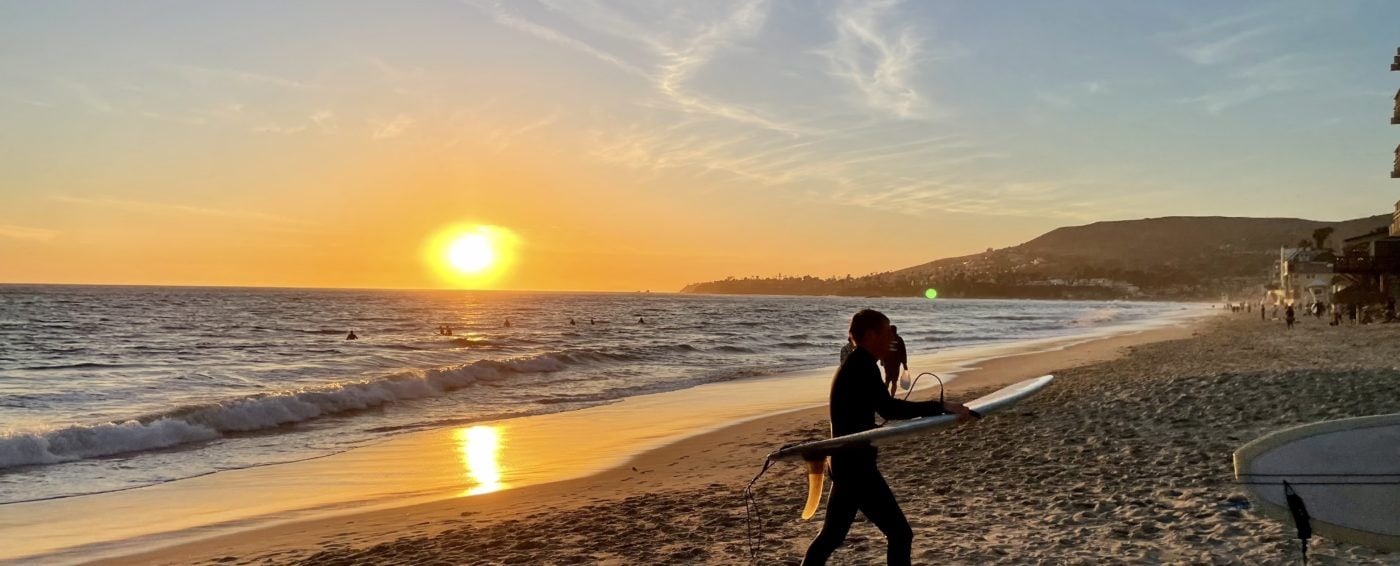 a surfer leaving laguna beach, california at sunset